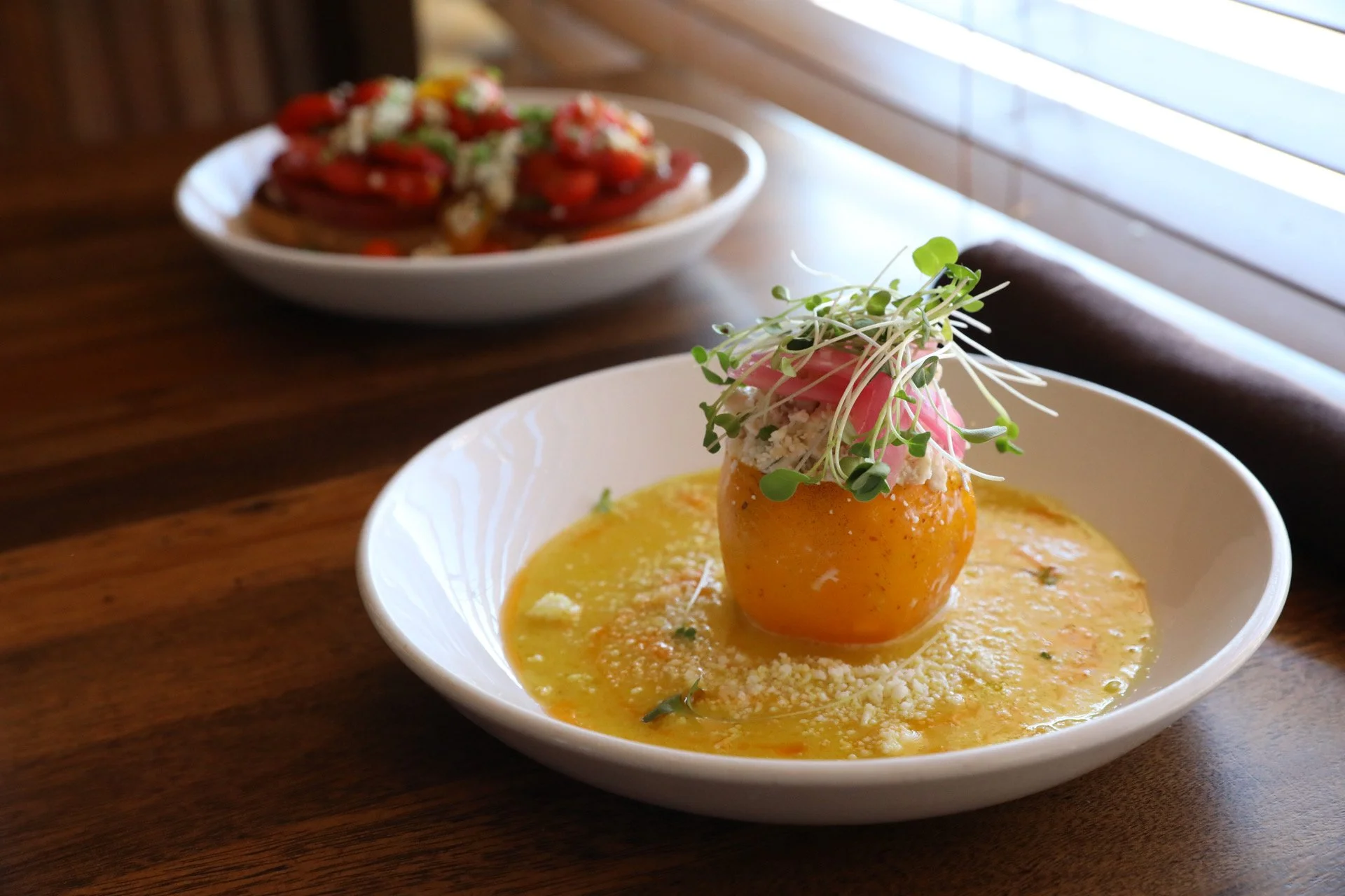 Crab-stuffed tomato in saffron broth, with heirloom tomato bruschetta in the background